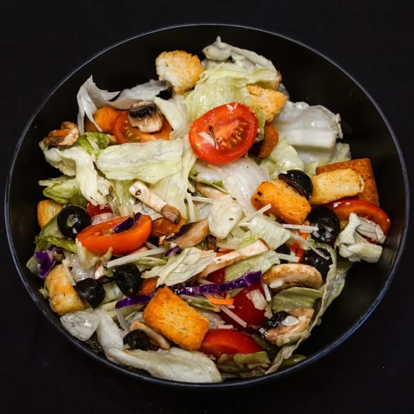A fresh garden salad in a black bowl, with lettuce, tomatoes, olives, mushrooms, and croutons.
