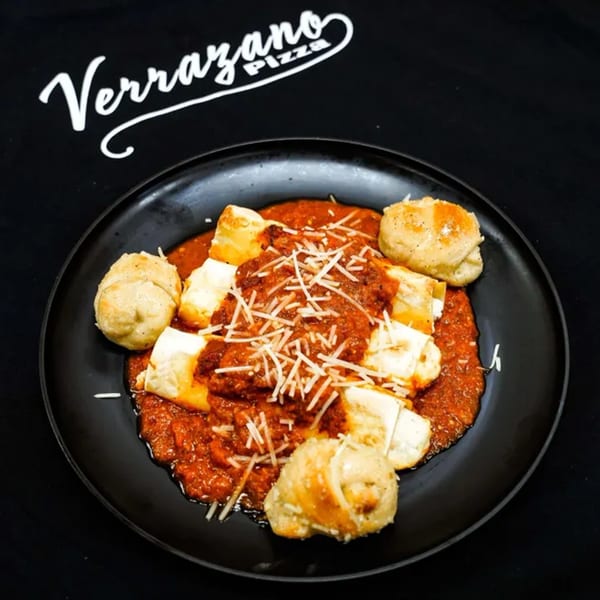 Baked ziti or lasagna with tomato sauce, melted cheese, and garlic knots on a black plate.