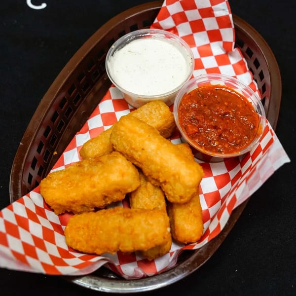 Golden-brown mozzarella sticks in a basket with red and white checkered paper, served with marinara and ranch.