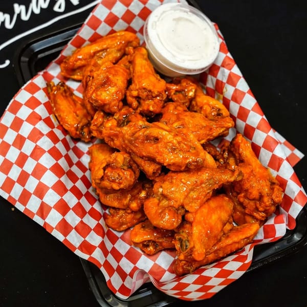 A black tray filled with buffalo chicken wings on red and white checkered paper, with a side of ranch.