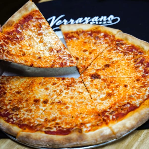 A hand lifts a slice of Verrazano Pizza's classic cheese pizza from a whole pie.